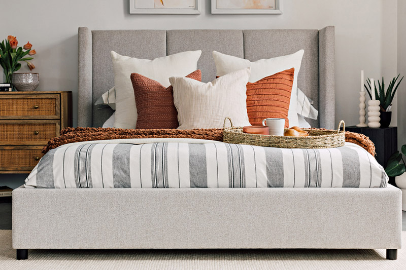 A well-made bed with striped sheets, orange throw pillows, and white pillows