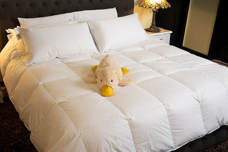 A stuffed animal duck lying on a soft whtite bed